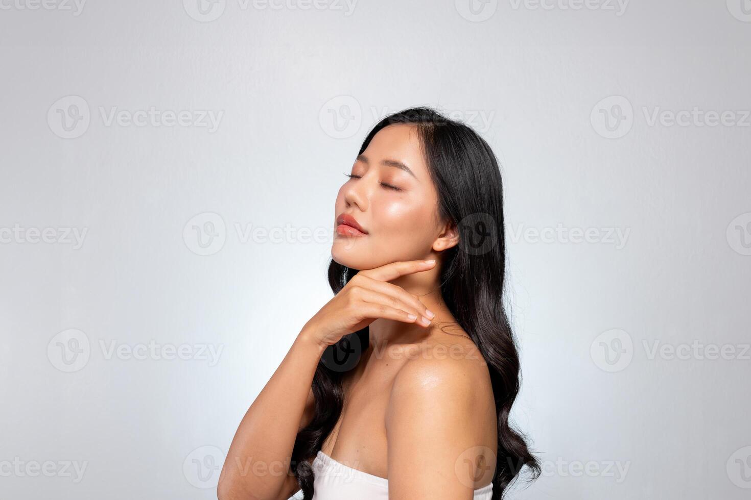 A young Asian beauty poses against a grey background, gently touching her face with her eyes closed. photo