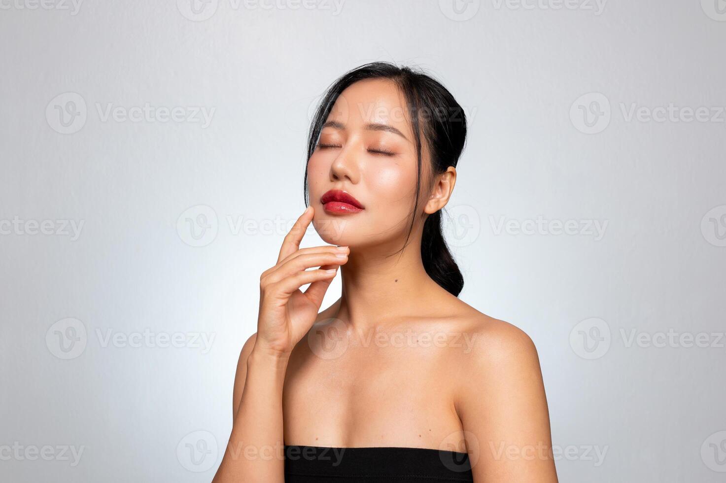 A young Asian woman with a perfect, beautiful face, touching her face with her eyes closed. photo