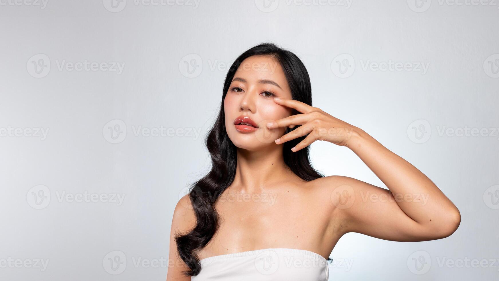 A gorgeous Asian woman poses against a grey background, touching her flawless facial skin. photo