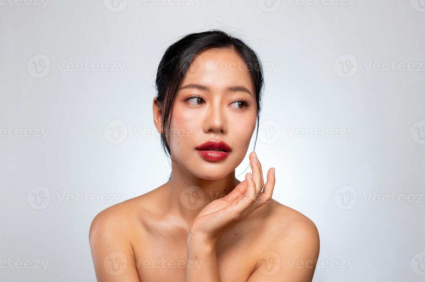 A beautiful Asian woman touches her chin while looking away, posing against a grey studio background photo
