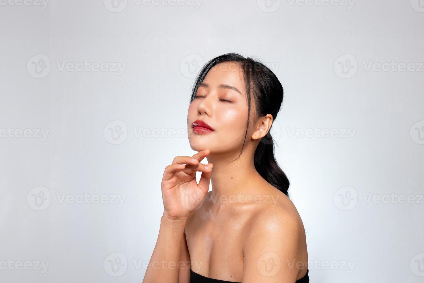 A young Asian woman with a perfect, beautiful face, touching her face with her eyes closed. photo
