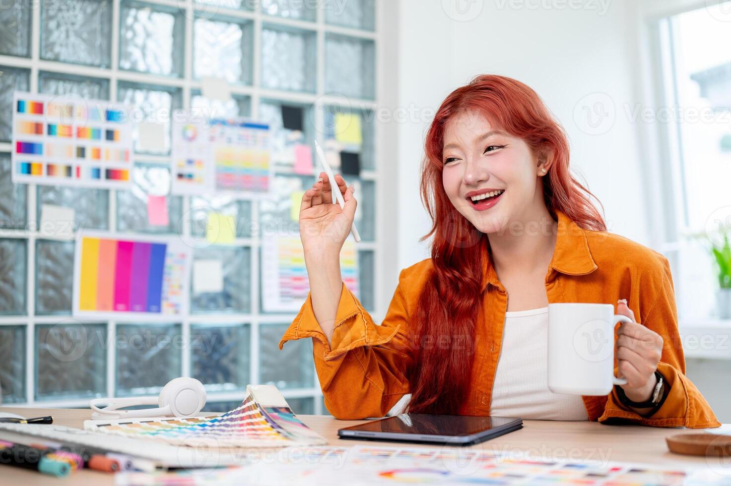 A cheerful Asian female graphic designer with red curly hair is smiling at the camera. photo
