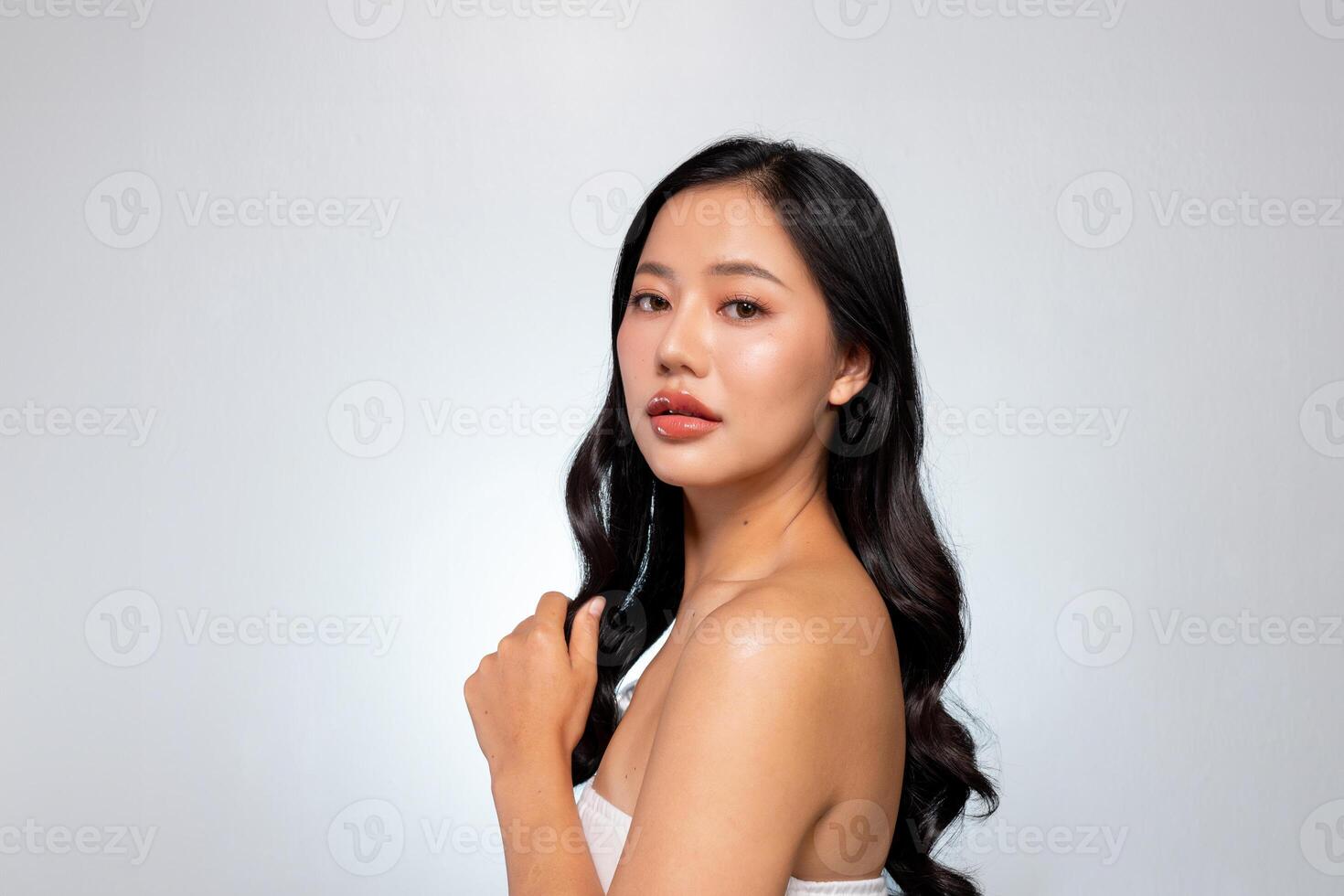 Gorgeous Asian woman poses against a grey background, showing her shoulder and looking at the camera photo