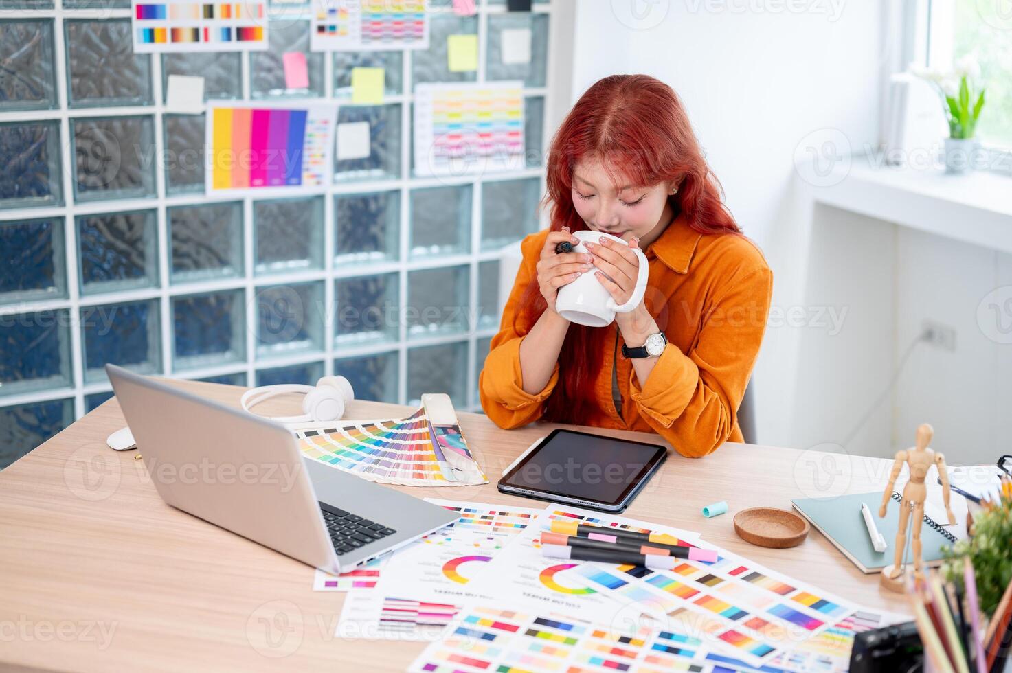A relaxed Asian female graphic designer is enjoying a morning coffee while working at her desk. photo