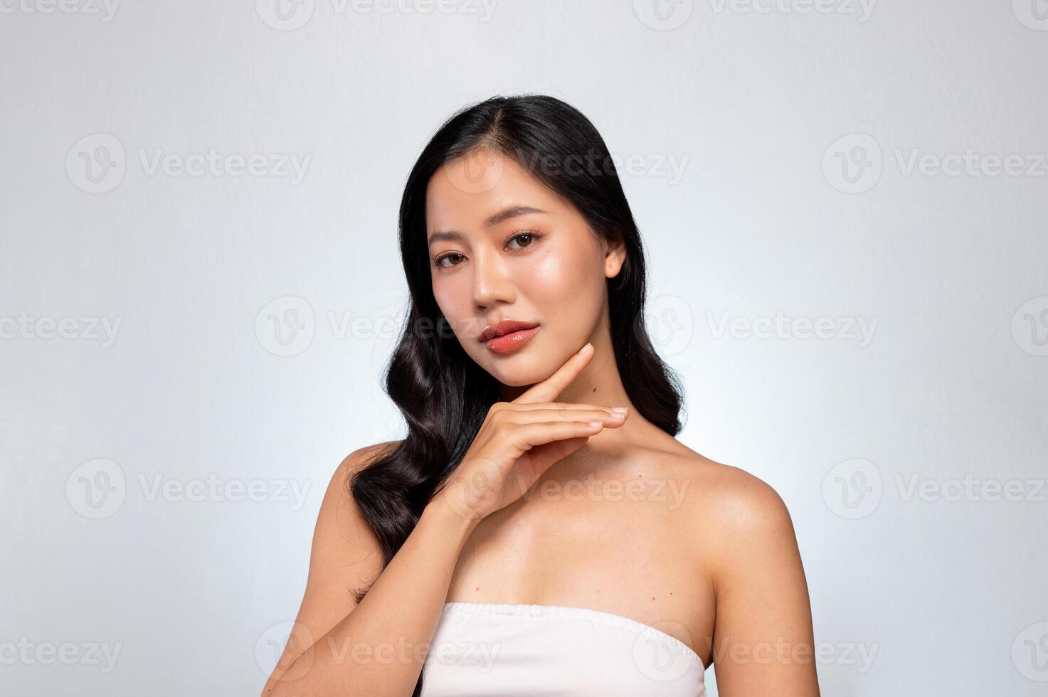 Gorgeous Asian woman with a beautiful face poses against a grey background, gently touching her chin photo
