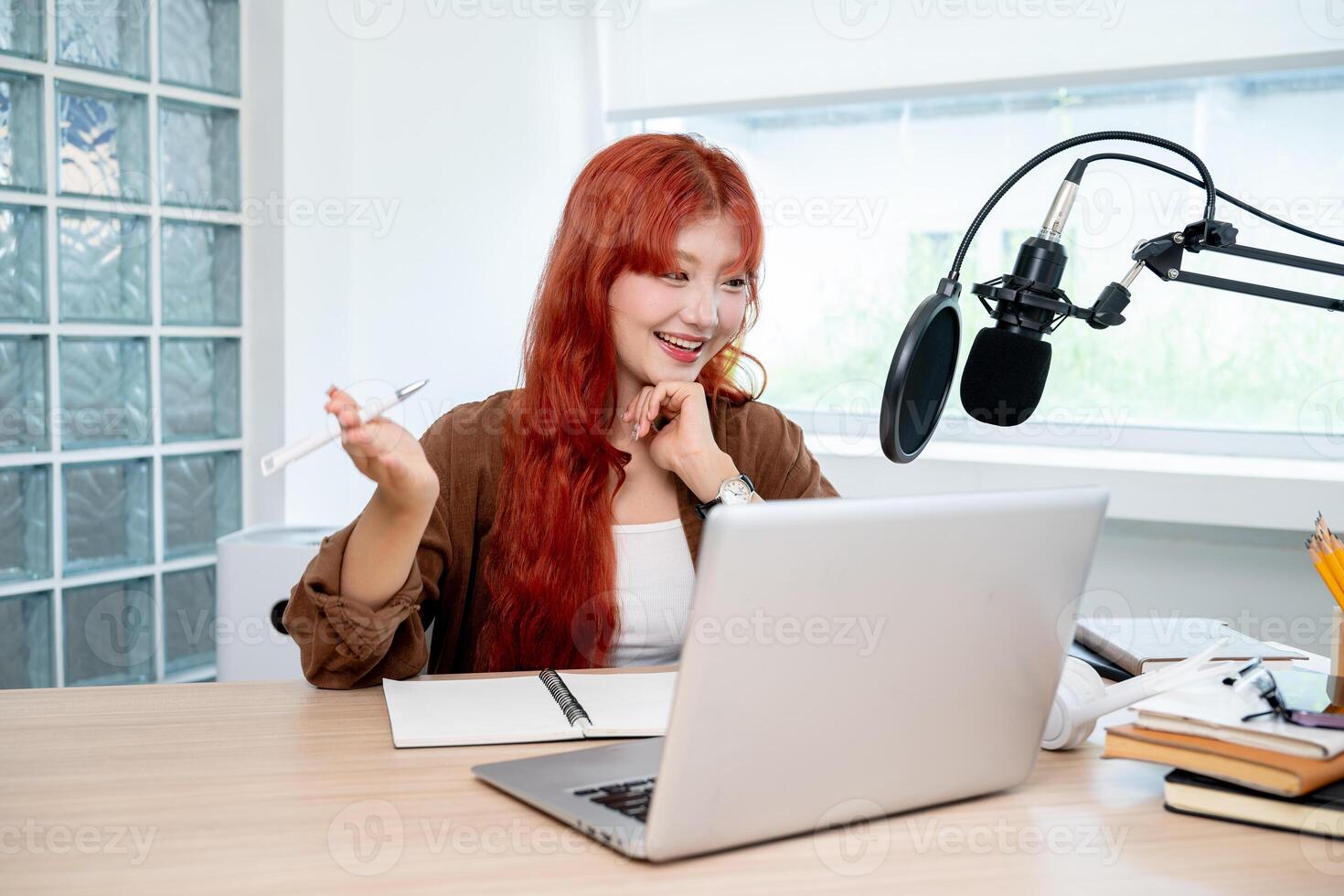 A smiling Asian female radio host or podcaster is working in her studio, speaking into the mic. photo