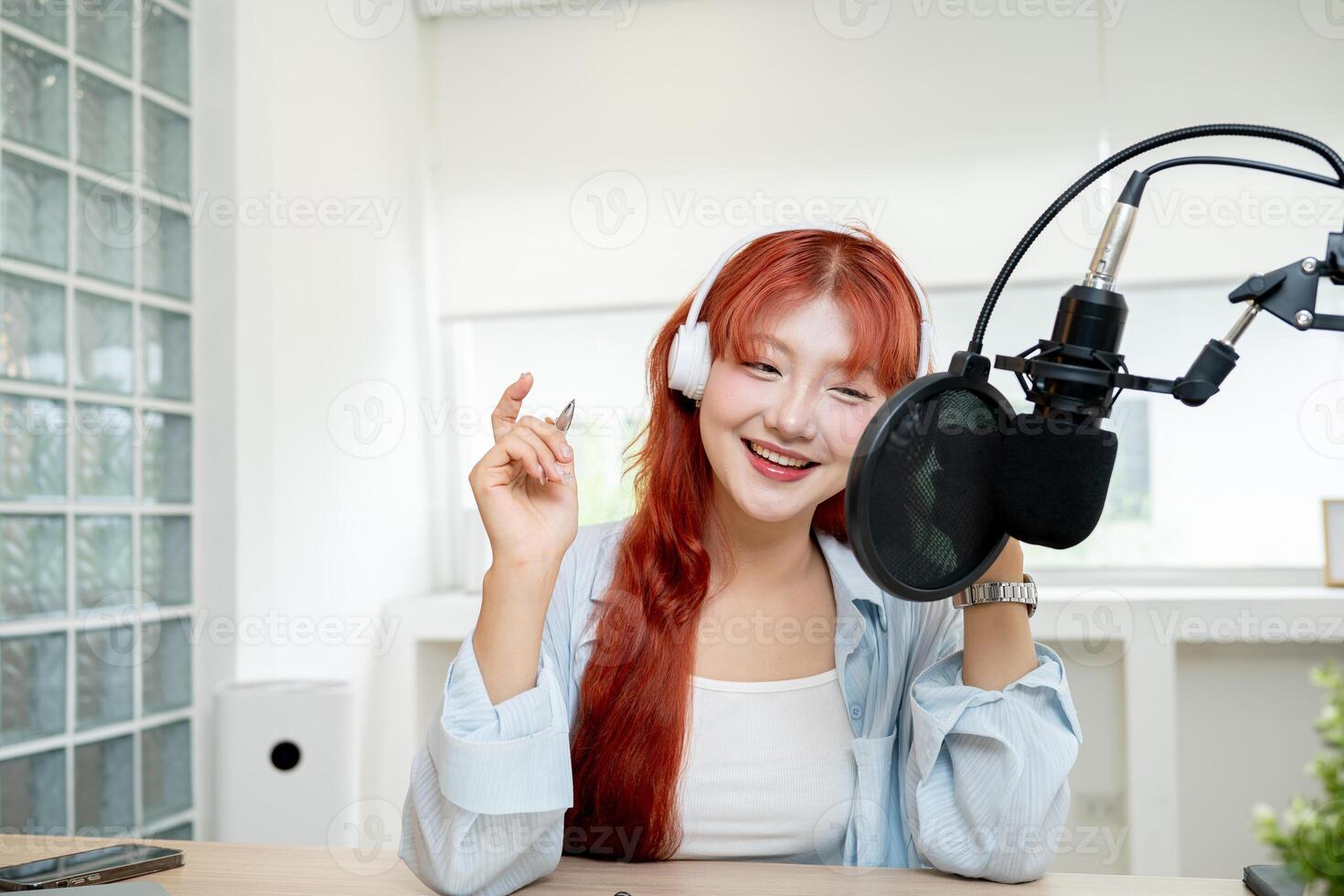 A smiling Asian female radio host or podcaster is working in her studio, speaking into the mic. photo