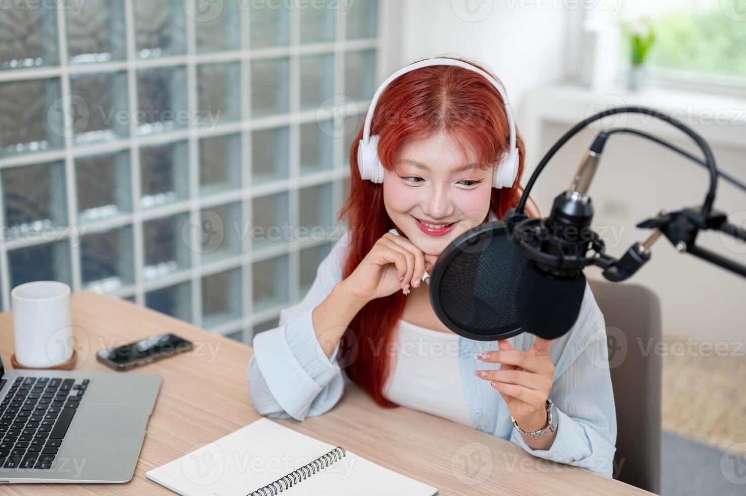 A beautiful Asian female podcaster is recording her podcast in the studio, speaking into a mic. photo