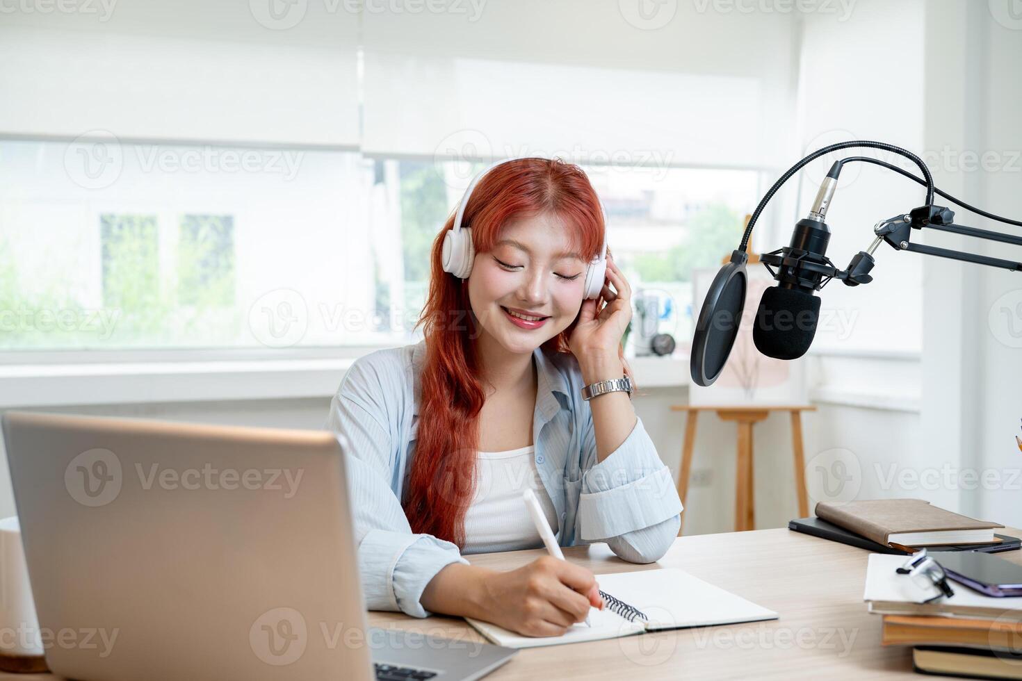 Attractive Asian female podcaster or radio journalist with red curly hair is working in her studio photo