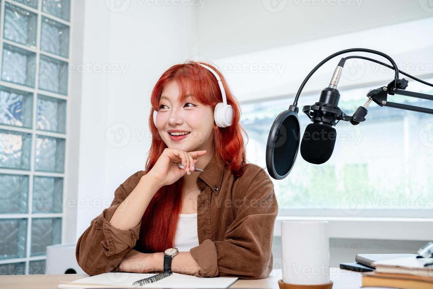 A beautiful Asian podcaster is in her studio, looking away and smiling with a dreamy expression. photo