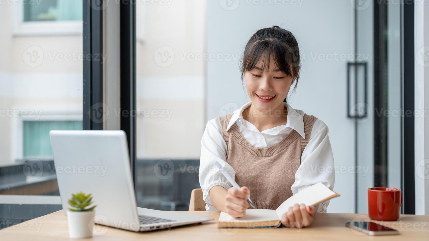An Asian female college student is lecturing in a book while studying an online class via her laptop photo