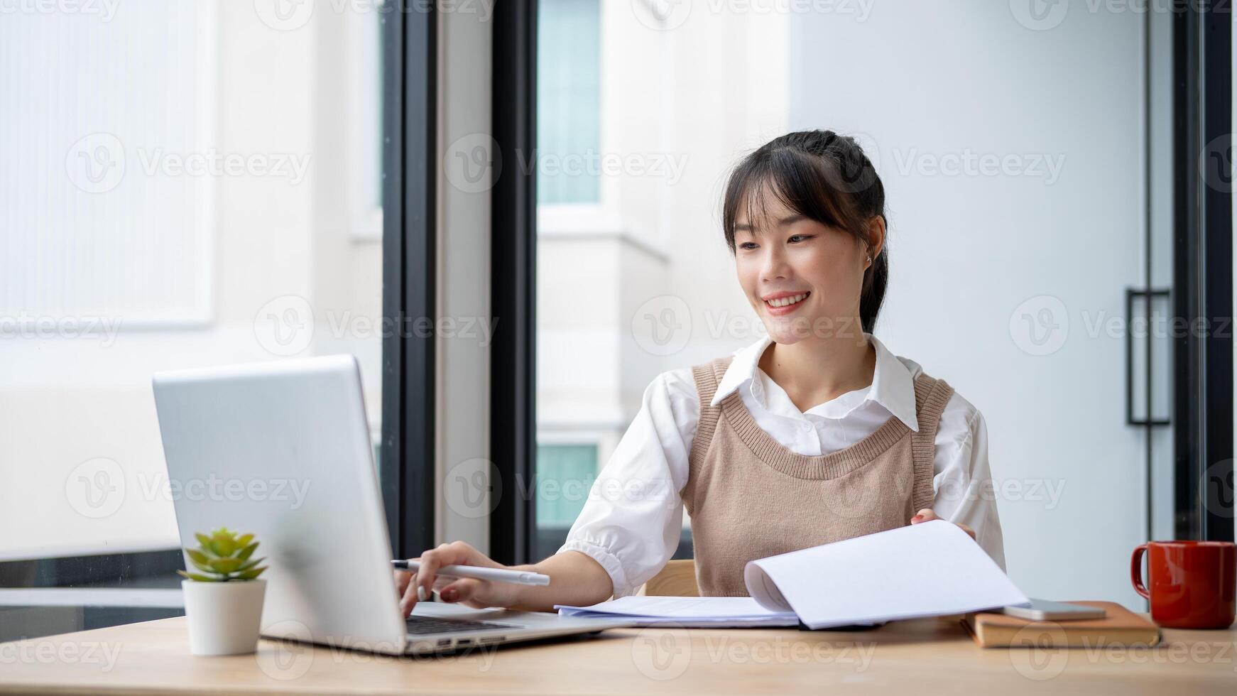 An Asian businesswoman is working at her desk, reviewing business report and working on her laptop. photo