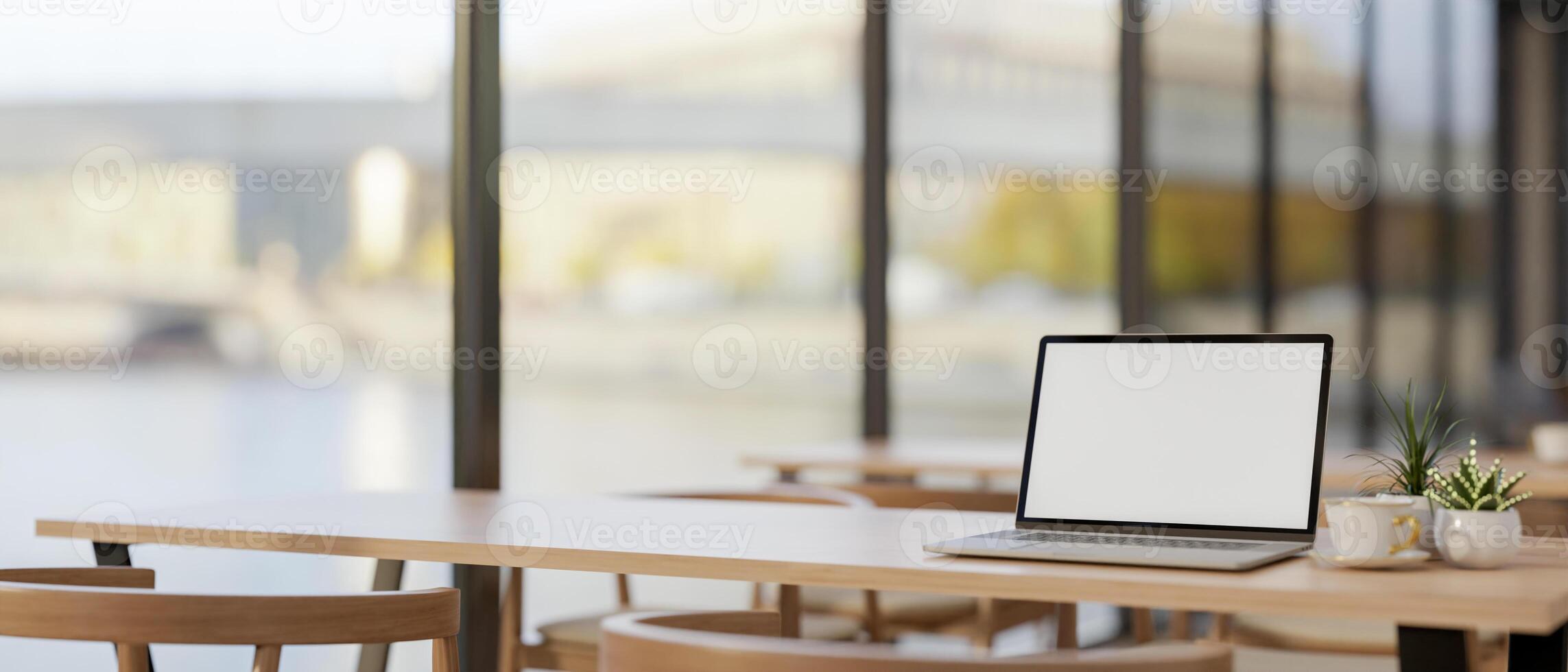 A laptop computer mockup on a wooden table by the window in a modern coffee shop co-working space. photo