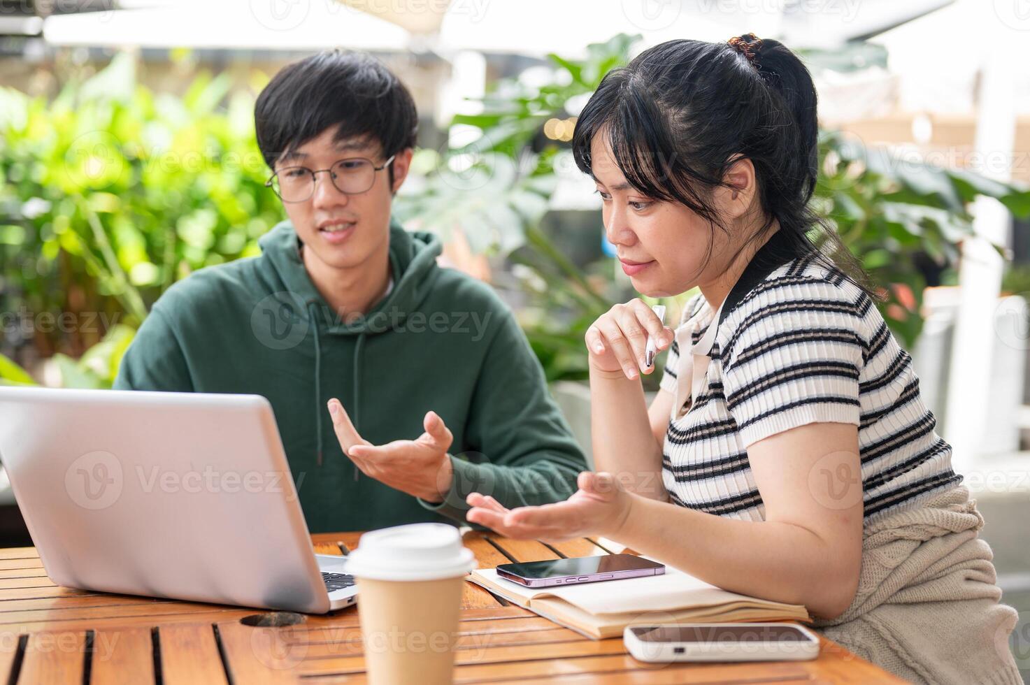 A positive Asian woman is working on a co-project with her friend, showing something on her laptop. photo