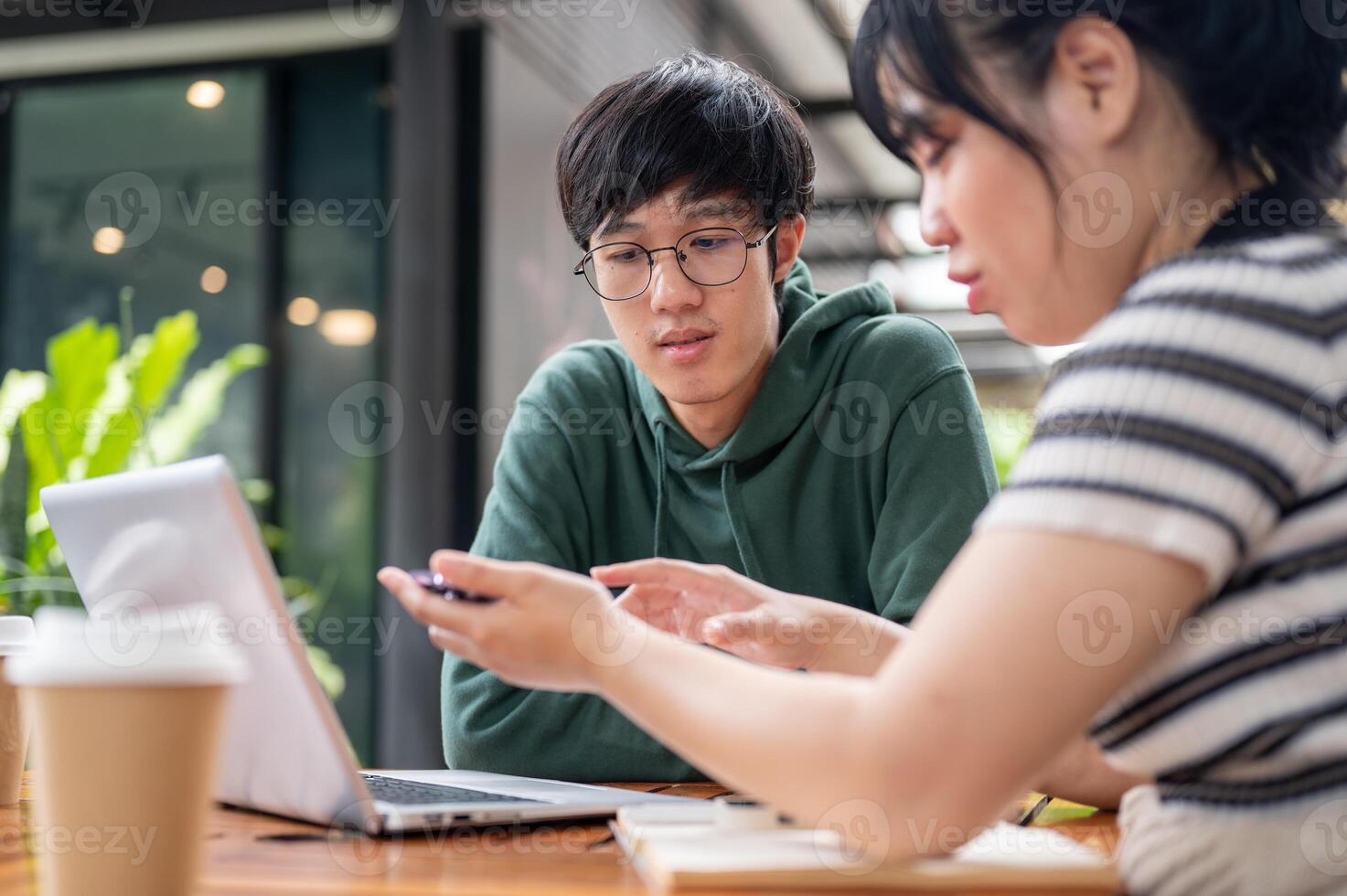 A young Asian man in a green hoodie listening to his friend explain something on her smartphone. photo