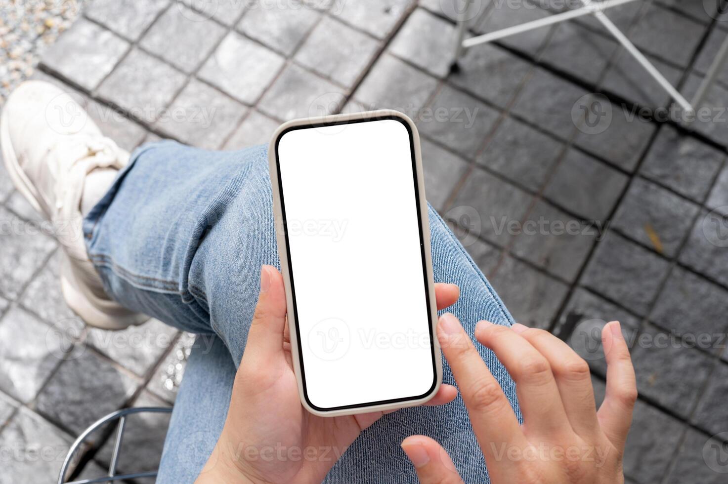 Top view image of a woman in jeans sitting outdoors, using her smartphone, touching on the screen. photo