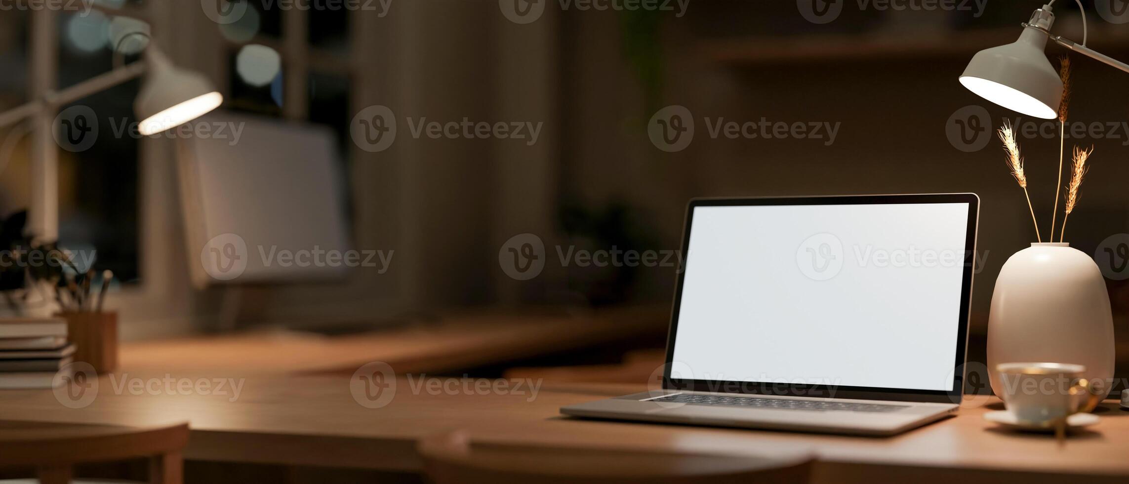 A laptop computer mockup on a wooden table in an office at night, illuminated by table lamps. photo