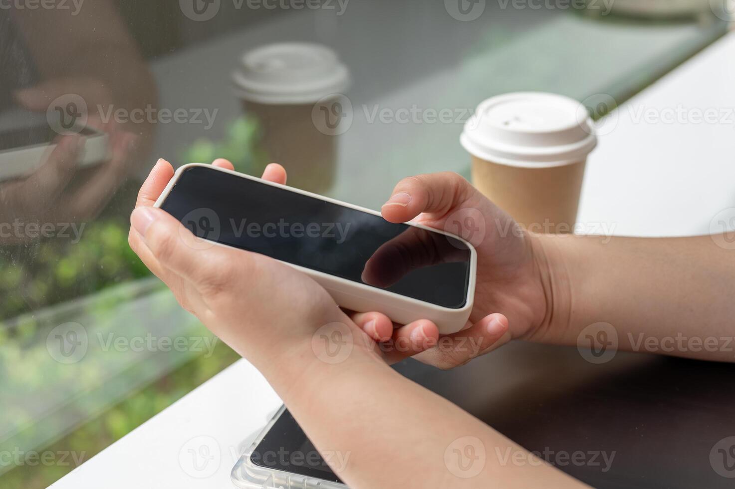 A close-up side view image of a woman using her smartphone while sitting in a coffee shop. photo