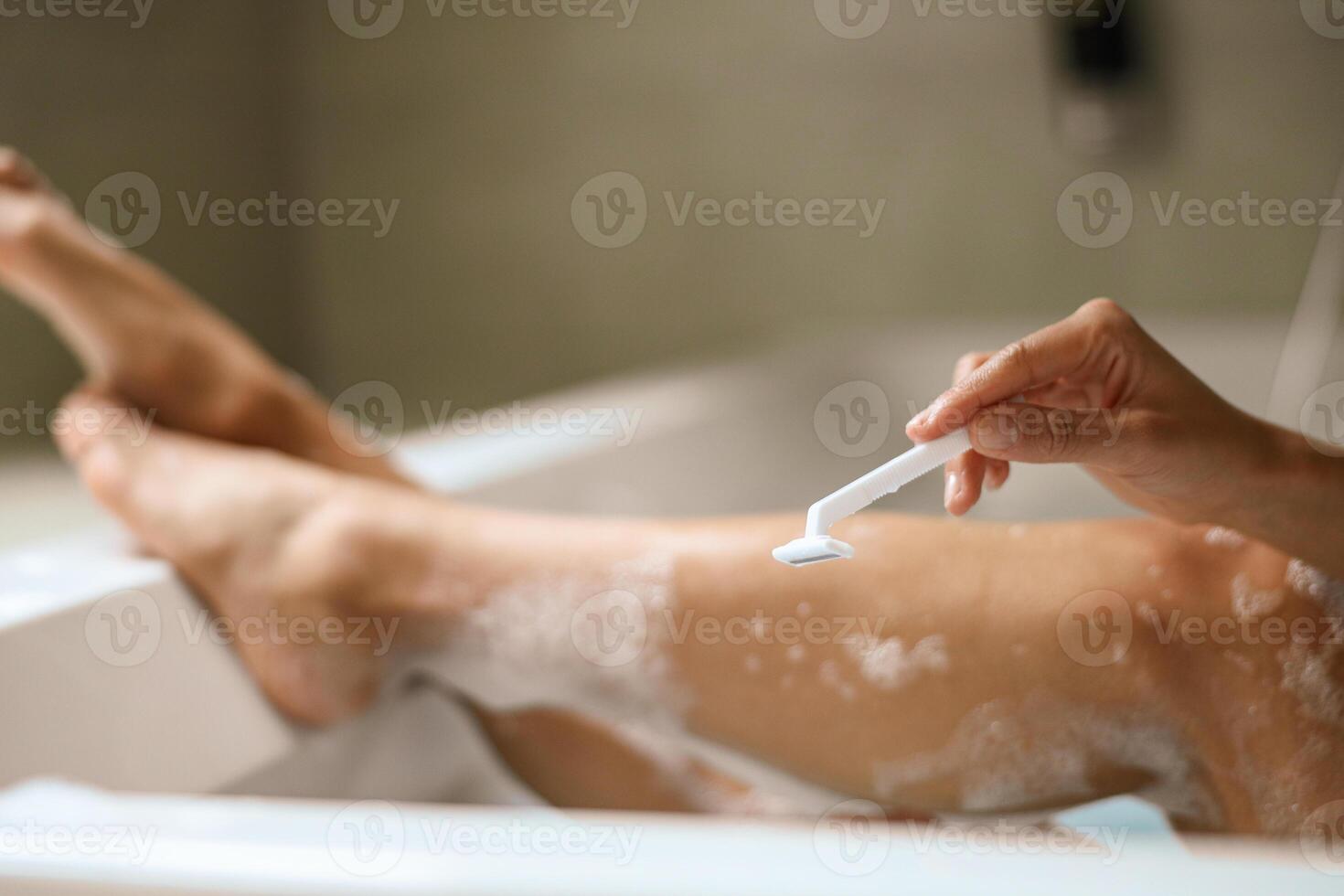 A woman is using a razor to shave her legs in a bathtub photo