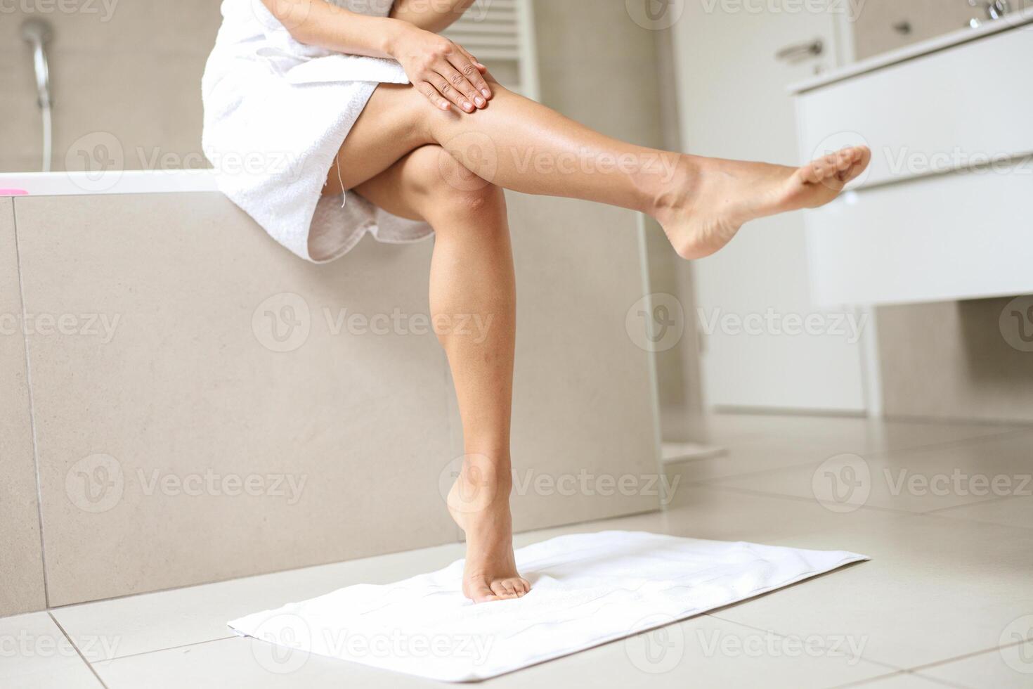 A woman is seated on a bathtub, with her legs crossed photo
