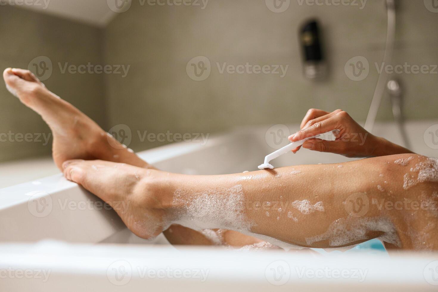 A woman is shaving her legs while bathing in a tub made of hardwood photo