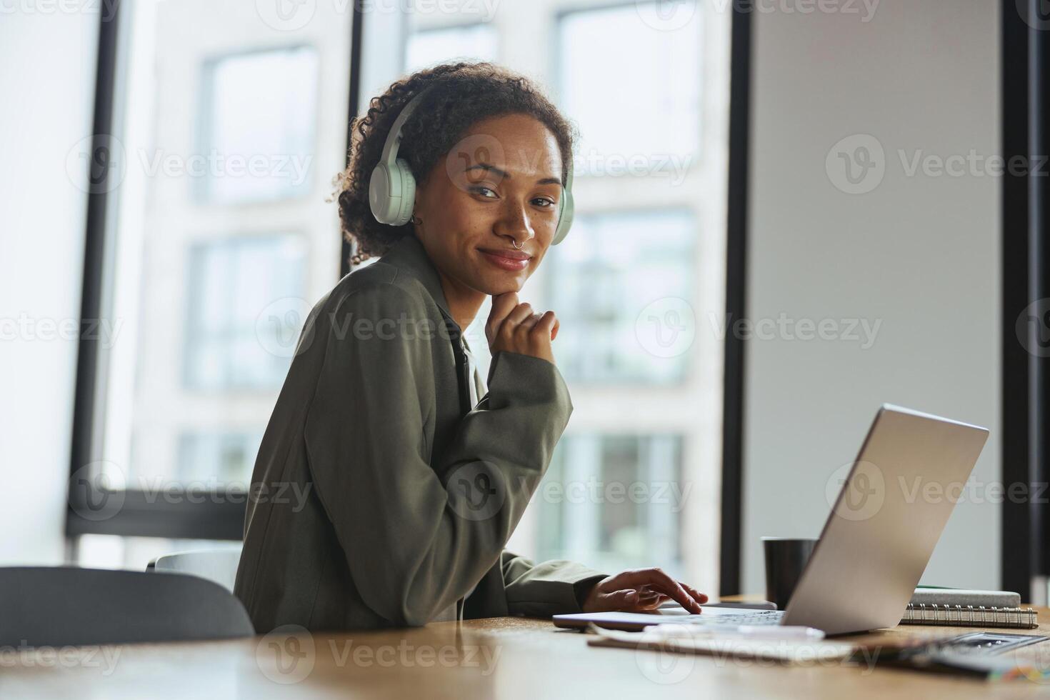 A woman at a desk with headphones using laptop computer in nice modern coworking office photo