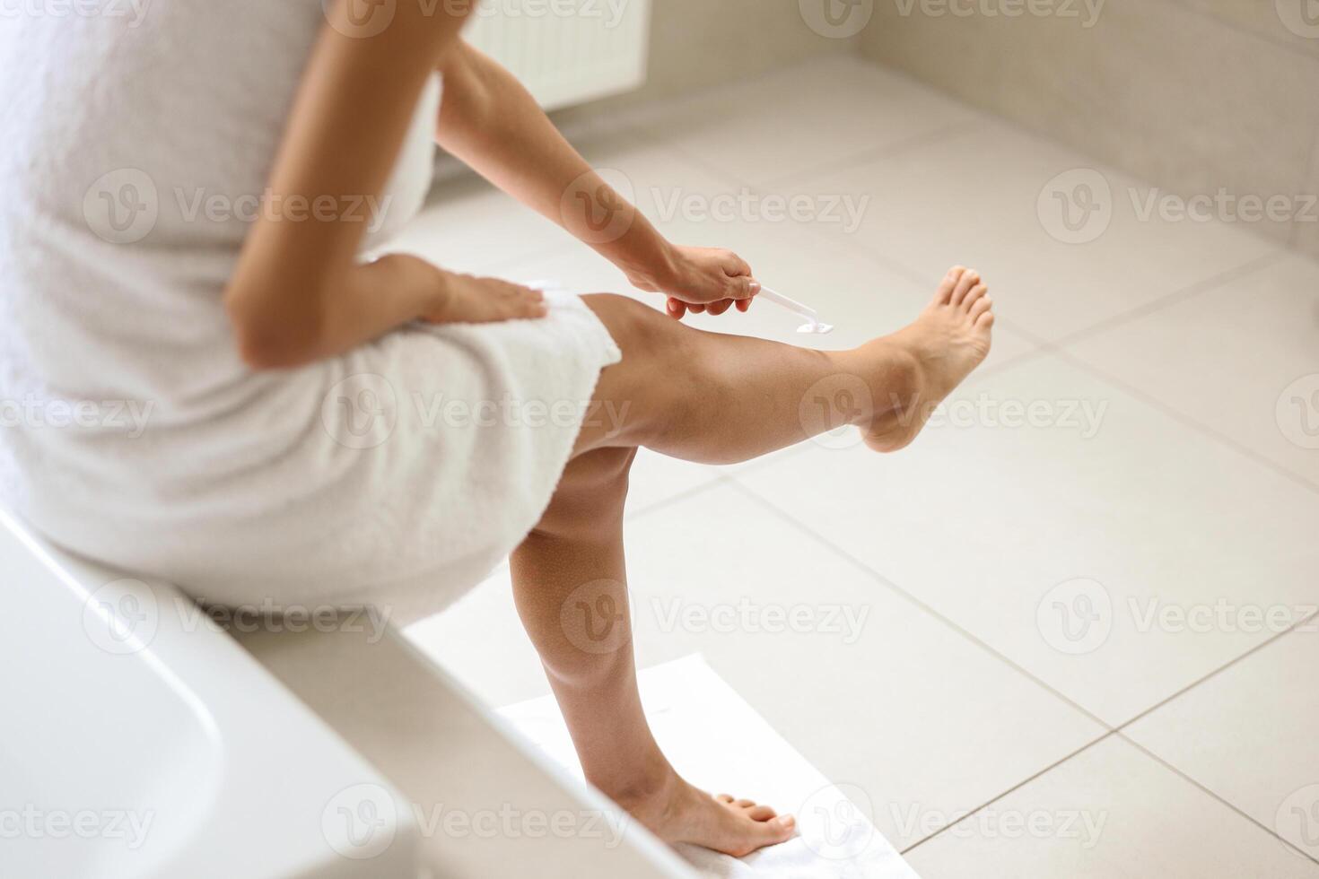 A woman sits by a window shaving her leg on hardwood flooring photo