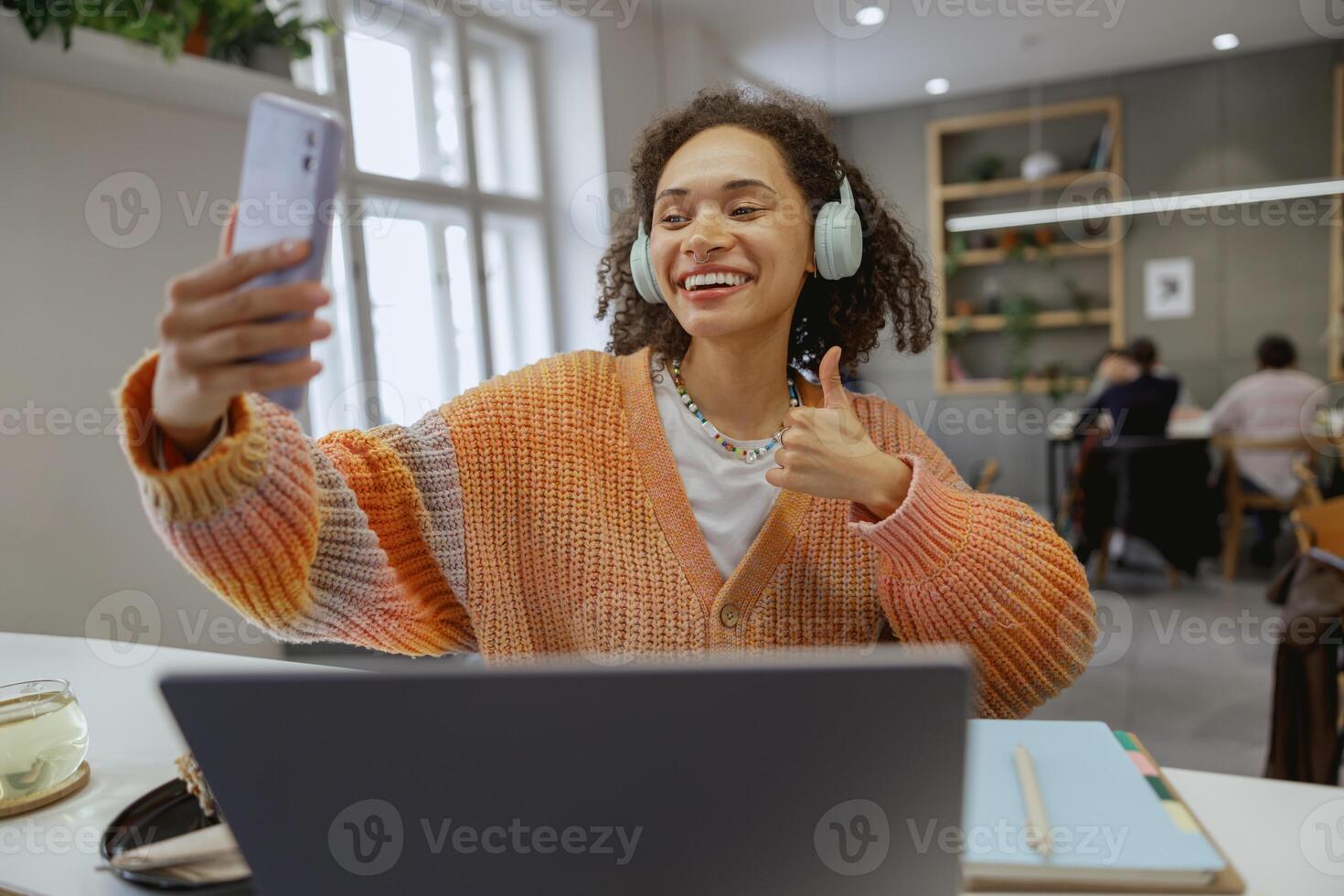 A woman with headphones capturing a selfie at a desk with a laptop and smiling photo