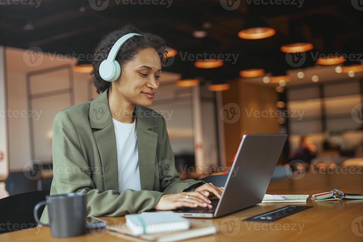 Woman iusing personal computer with headphones at table in nice modern coworking office photo