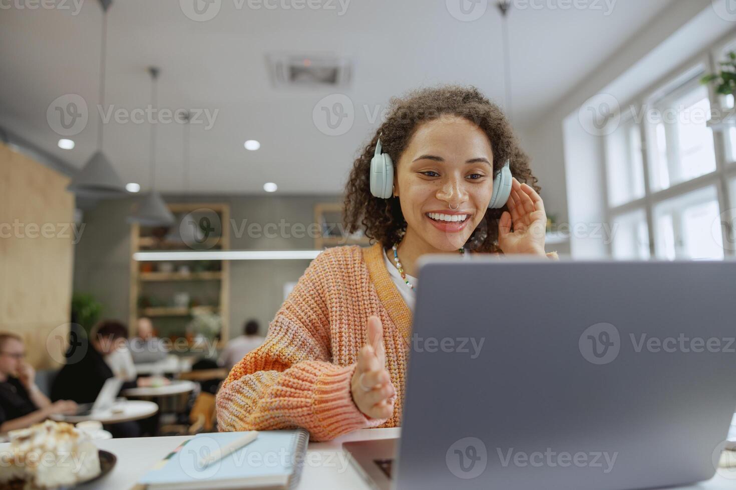 A woman at her desk in front of a laptop computer with headphones, smiling in a cozy minimalistic cafe photo