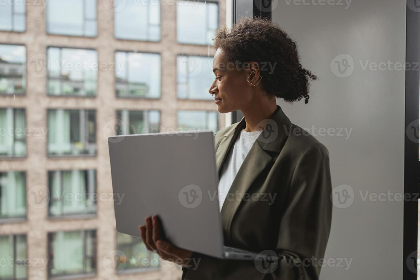 a woman is standing in front of a window holding a laptop computer photo