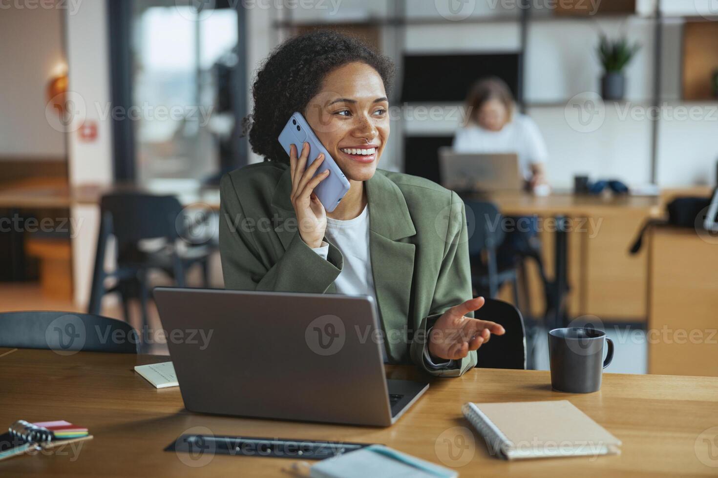 A whitecollar worker sits at a desk with a laptop and talks on a cell phone in nice modern coworking office photo