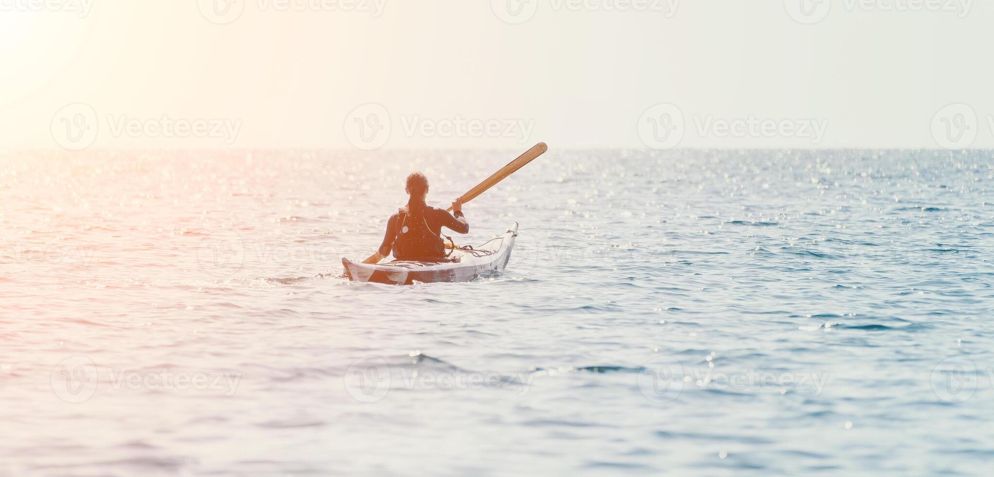 Woman sea kayak. Happy smiling woman in kayak on ocean, paddling with wooden oar. Calm sea water and horizon in background. Active lifestyle at sea. Summer vacation. photo