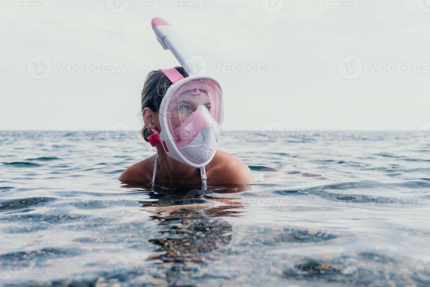Young happy woman in white bikini and wearing pink mask gets ready for sea snorkeling. Positive smiling woman relaxing and enjoying water activities with family summer travel holidays vacation on sea. photo