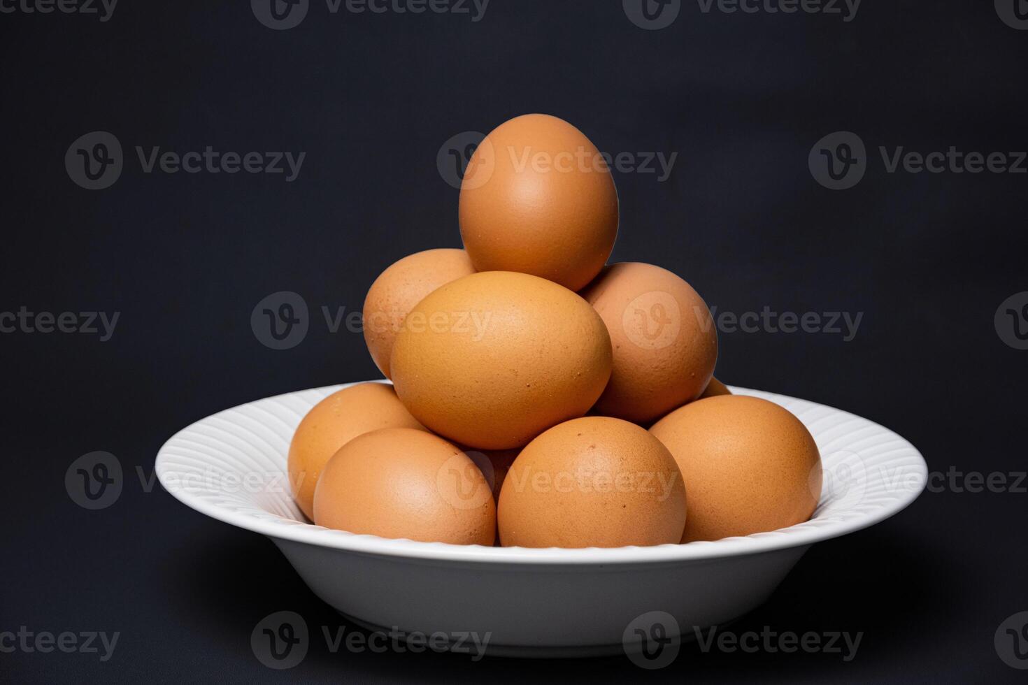 White plate with arrangement of raw chicken eggs isolated on black background. Raw chicken eggs for cooking purposes. photo