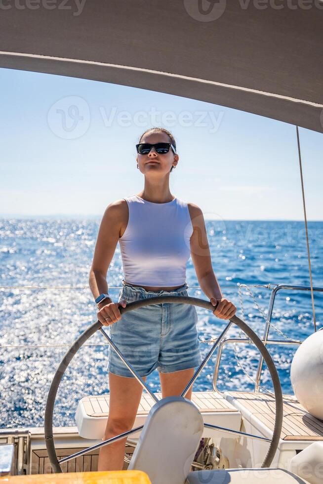 Young woman female captain stands at the helm and controls a sailboat during a journey by sea. High quality photo