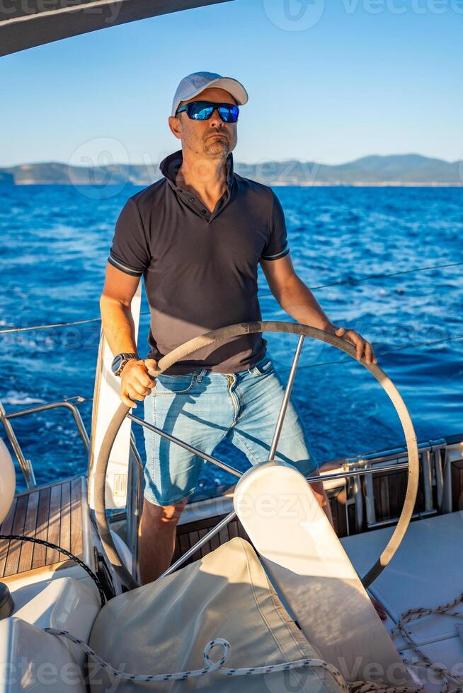 Young man captain stands at the helm and controls a sailboat during a journey by sea. High quality photo