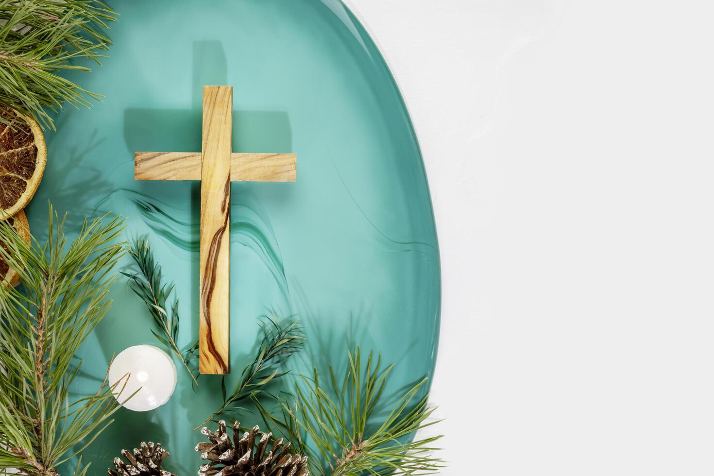Wood cross with fir branches, cones, candle and dry oranges photo