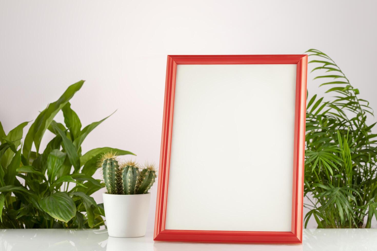 Home plantes and empty picture frame mockup on white desk photo