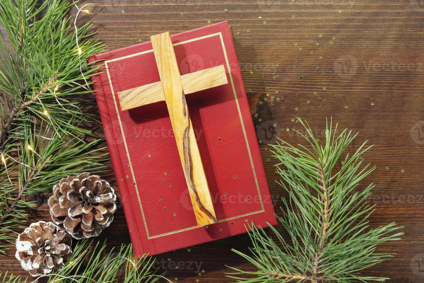 Wood cross laying on a closed red Christian bible with fir branches and cones photo