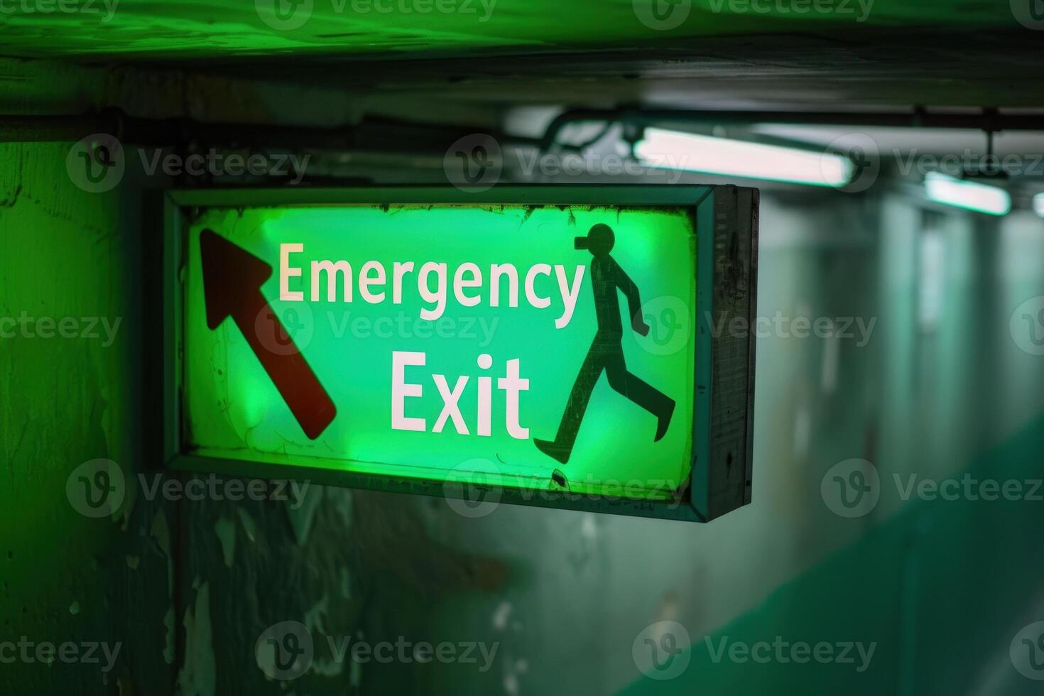 A vibrant green emergency exit sign shines brightly, directing individuals towards safety in a shadowy corridor. photo