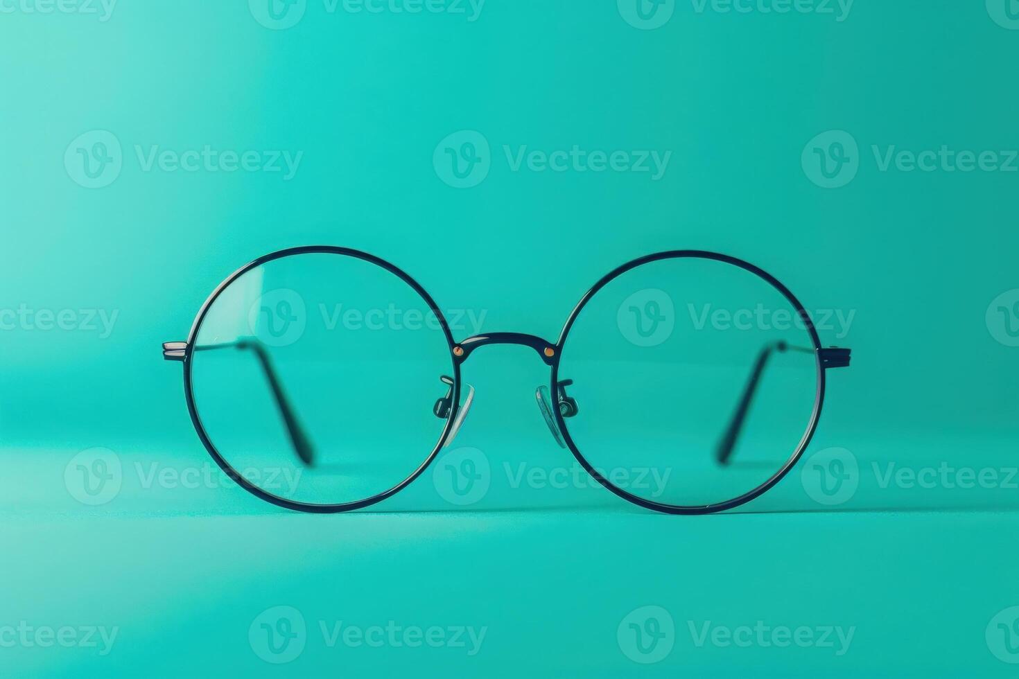 A stylish pair of round glasses rests on a bright turquoise surface, showcasing their sleek design and modern aesthetic. photo