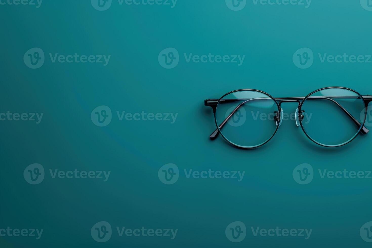 A chic pair of contemporary glasses lies gracefully on a striking teal backdrop, showcasing its elegant design. photo