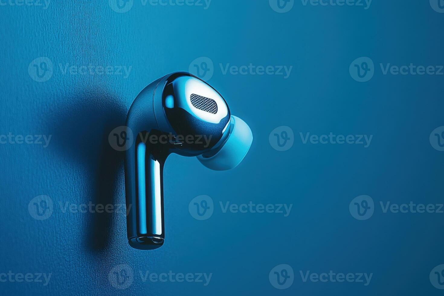 A stylish wireless earbud floats effortlessly, reflecting light in a captivating blue setting, embodying modern design and technology. photo