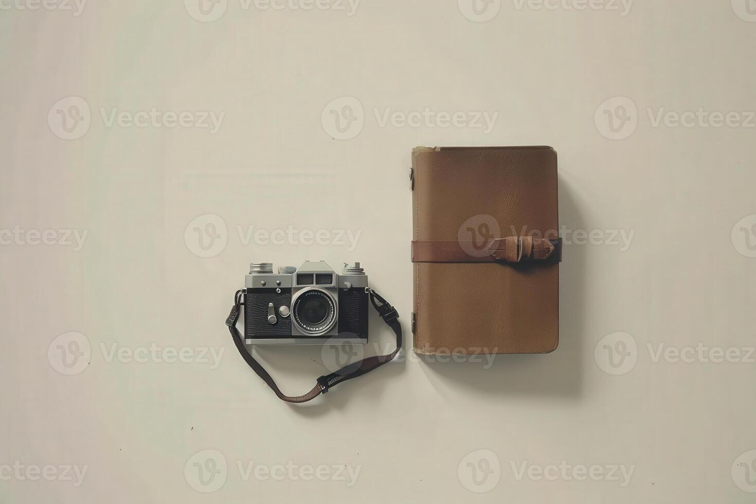 A vintage camera rests beside a well-worn travel journal, inviting memories and adventures on a neutral surface. photo