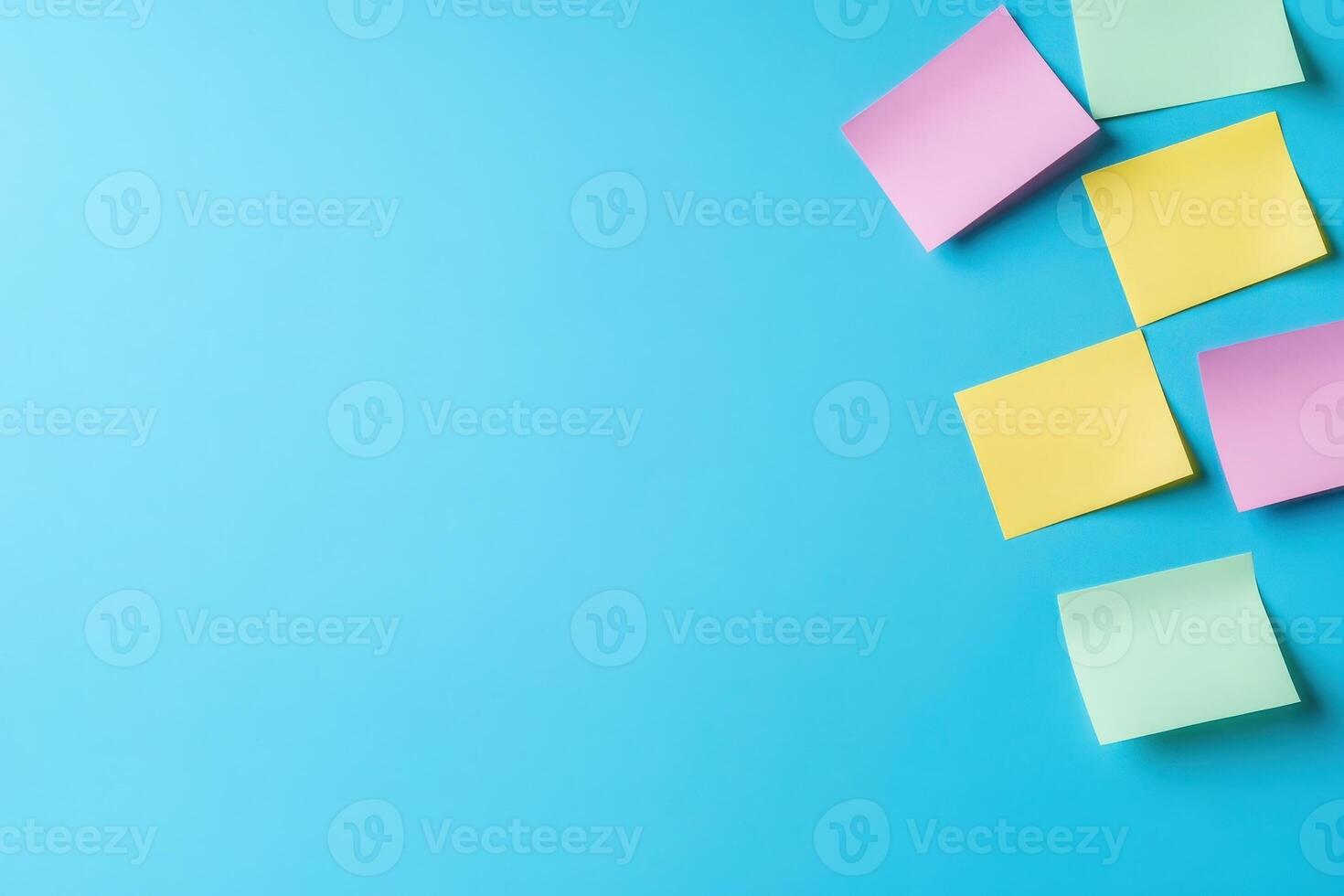 A collection of colorful sticky notes in pink, yellow, and green positioned creatively against a solid blue backdrop. photo