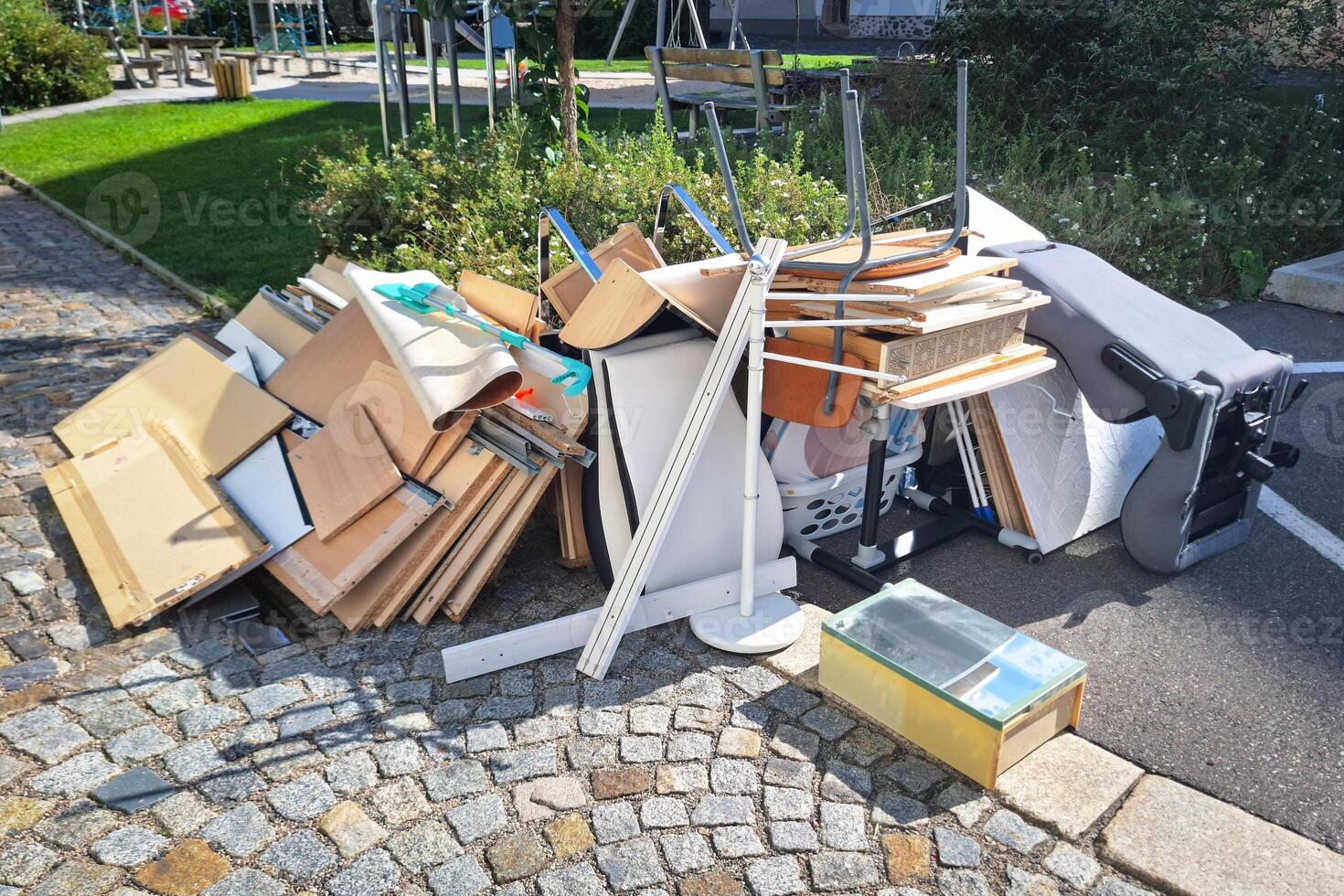 A heap of assorted discarded household items and furniture piled up on a cobblestone street, depicting a bulk waste collection day in an urban environment. photo