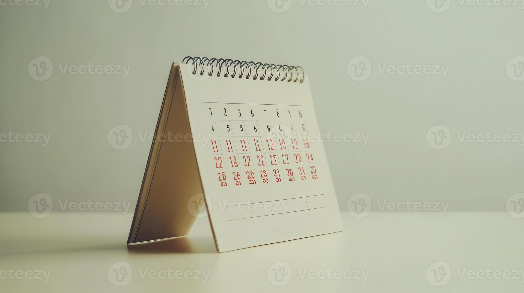 A small, spiral-bound desk calendar displaying the days of the month on a minimalist surface in a bright, natural light setting photo