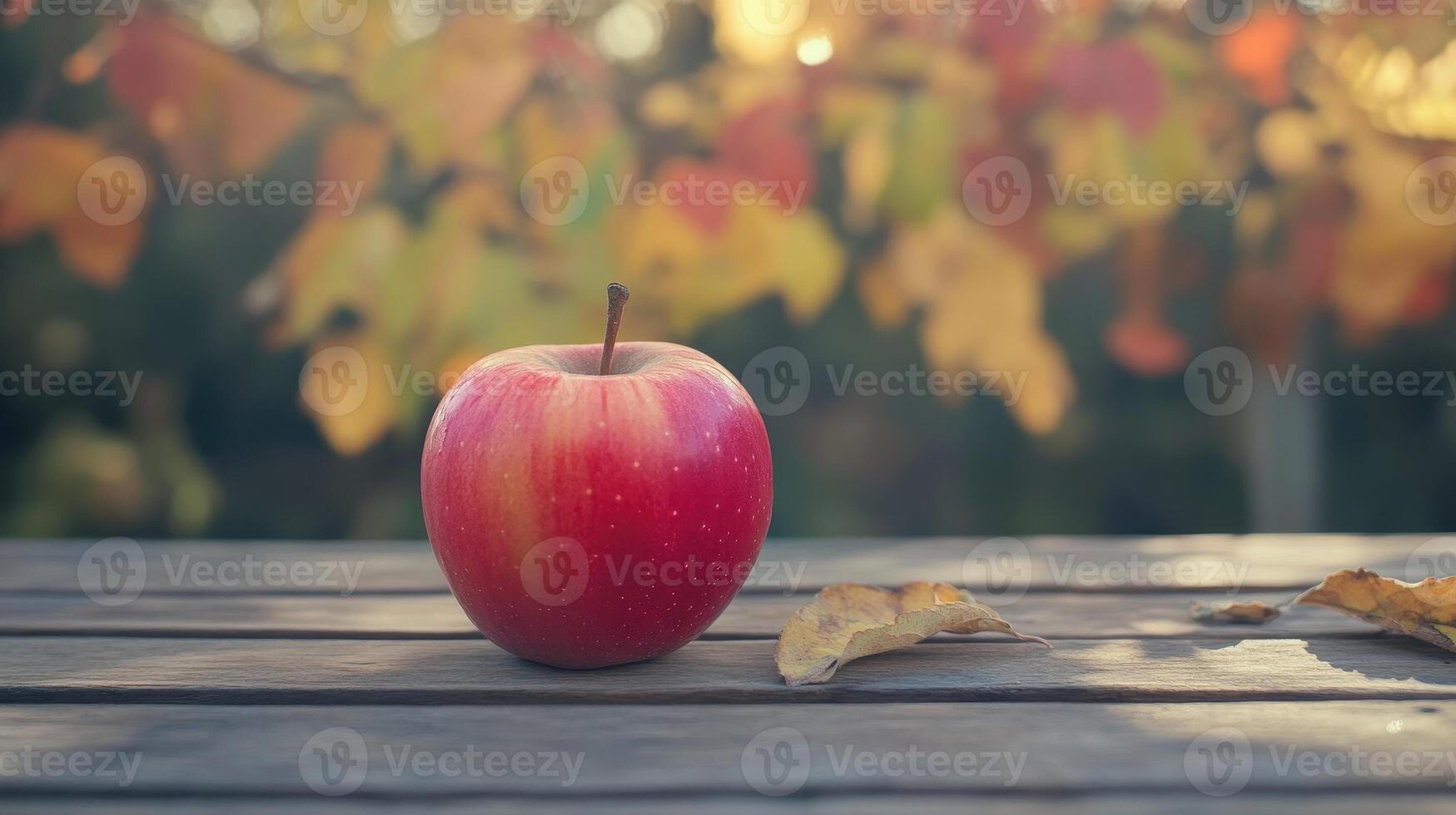 Fresh Red Apple Resting on Wooden Table Surrounded by Colorful Fall Leaves in Late Afternoon Light photo