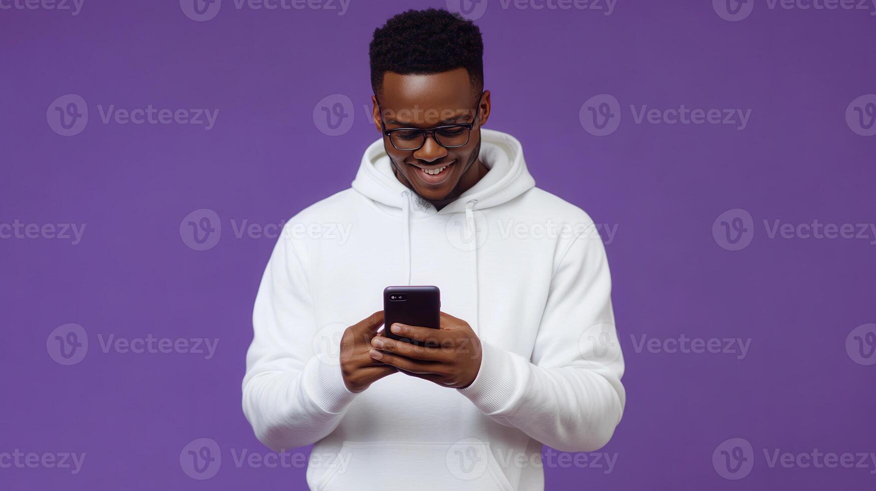 Young man in a white hoodie smiles while using a smartphone against a purple background photo